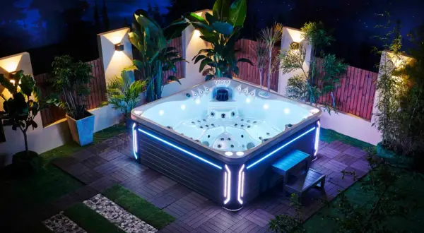 Nowoczesne spa do ogrodu, oświetlone nocą, otoczone roślinnością i drewnianym tarasem. Idealne miejsce na relaks pod gwiazdami.