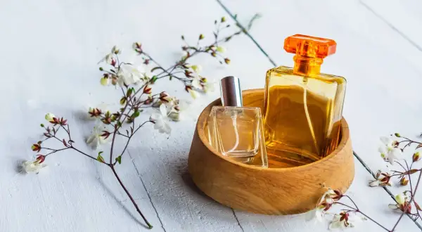 Dwie buteleczki perfum, jedna w szkle, druga w bursztynowym kolorze, w drewnianej miseczce, otoczone delikatnymi kwiatami. Czy to woda toaletowa czy tester?