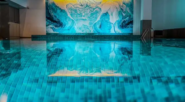 Relaks w nowoczesnym spa pod Poznaniem. Błękitna woda basenu odbija abstrakcyjną, turkusowo-żółtą mozaikę na ścianie.