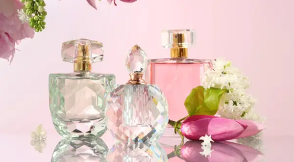 Eleganckie flakony perfum i wody toaletowej, otoczone kwiatami. Różnica między nimi tkwi w stężeniu olejków zapachowych.