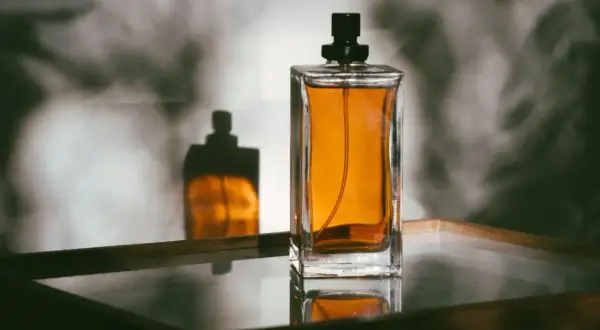 Elegancka butelka perfum z bursztynowym płynem i jej odbicie. Dowiedz się, jak przelać perfumy do innej butelki, by cieszyć się ulubionym zapachem.