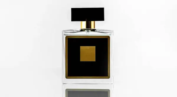 Elegancka szklana butelka perfum z czarną etykietą i złotym kwadratem.
