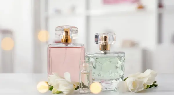 Szukasz inspiracji, jakie perfumy z Rossmanna polecacie? Na zdjęciu eleganckie flakoniki z różowymi i zielonymi perfumami, ozdobione białymi kwiatami.