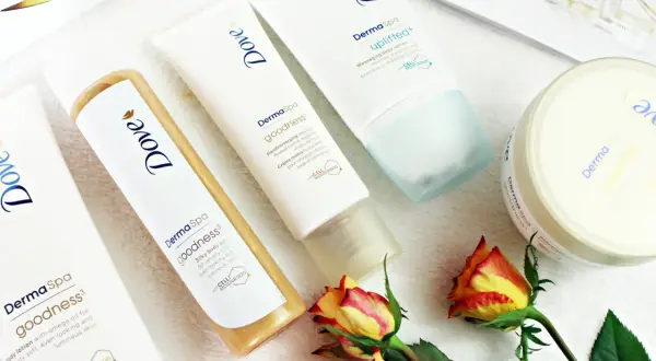 Krem do rąk, olejek i balsam do ciała z serii Dove DermaSpa Goodness, otoczone płatkami róż.