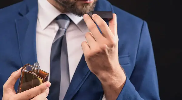 Elegancki mężczyzna w garniturze wącha perfumy, zastanawiając się, co mocniejsze: woda toaletowa czy perfumowana.